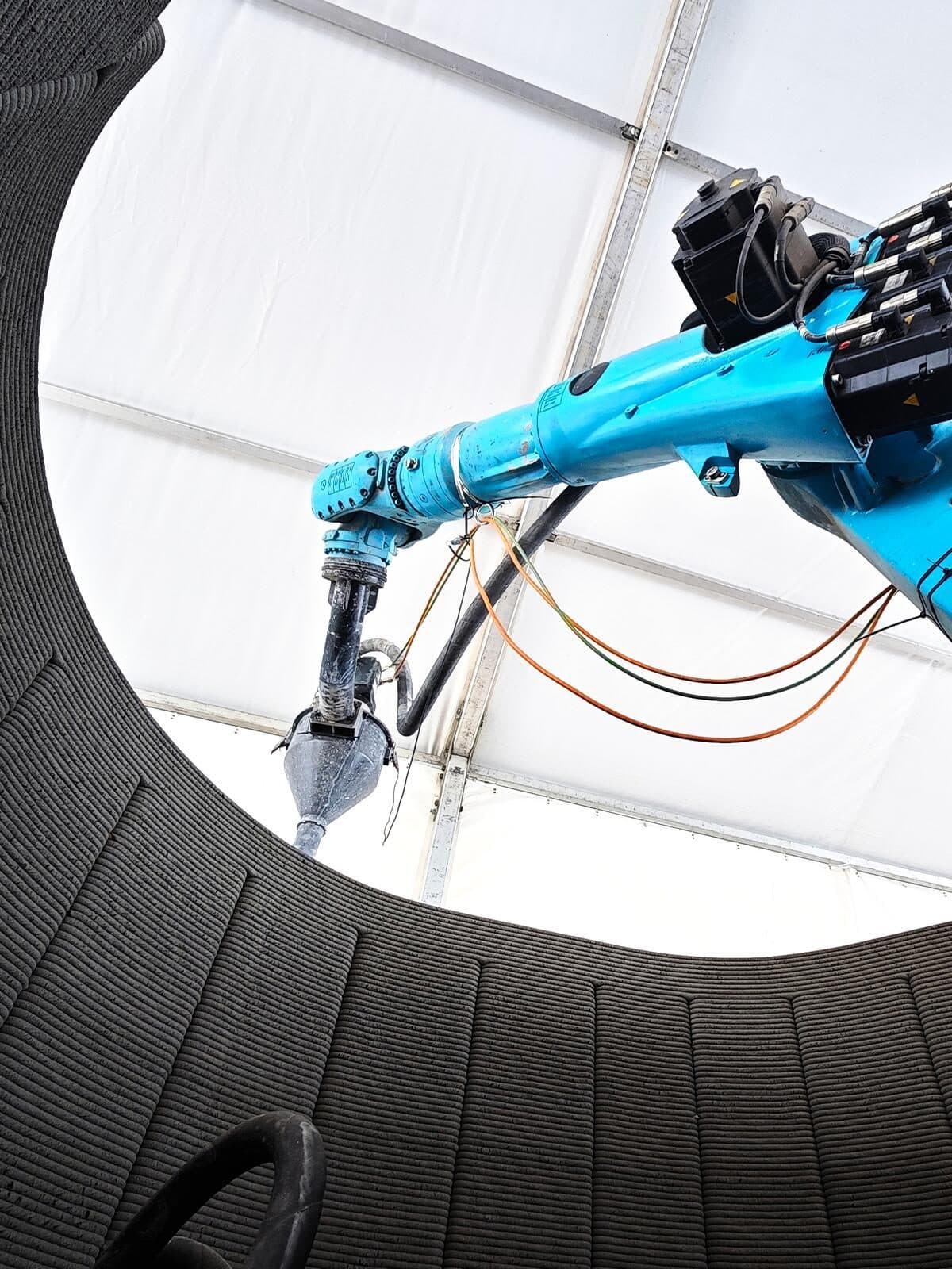 Robotic arm depositing layered material to form a curved wall, showing fine horizontal layer lines